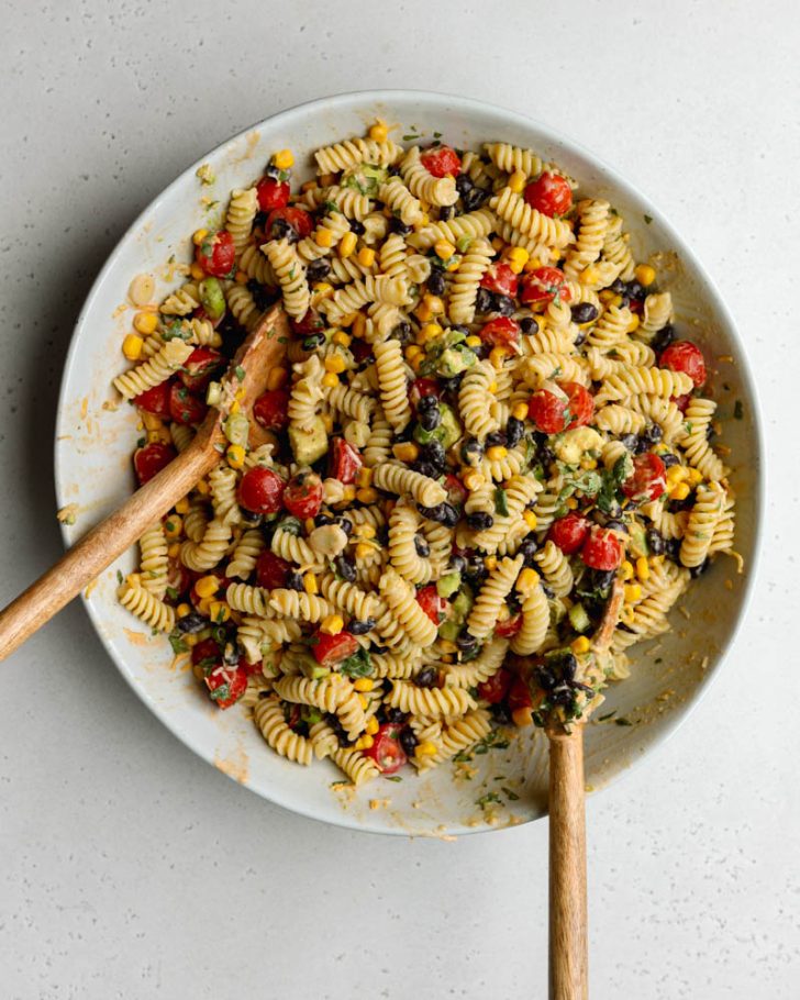 Large bowl of taco pasta salad mixed together with wooden salad spoons