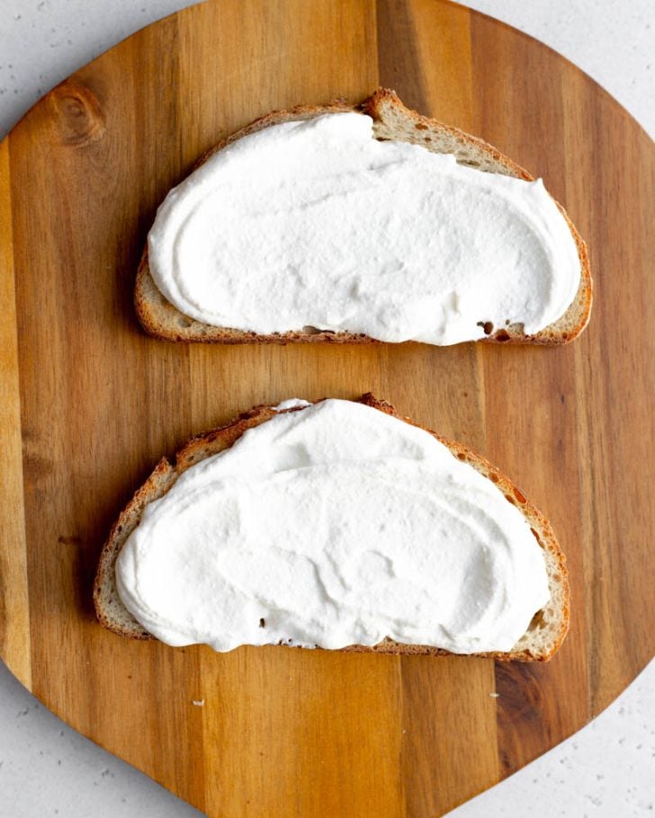 whipped cottage cheese spread onto two pieces of toast on a wooden cutting board