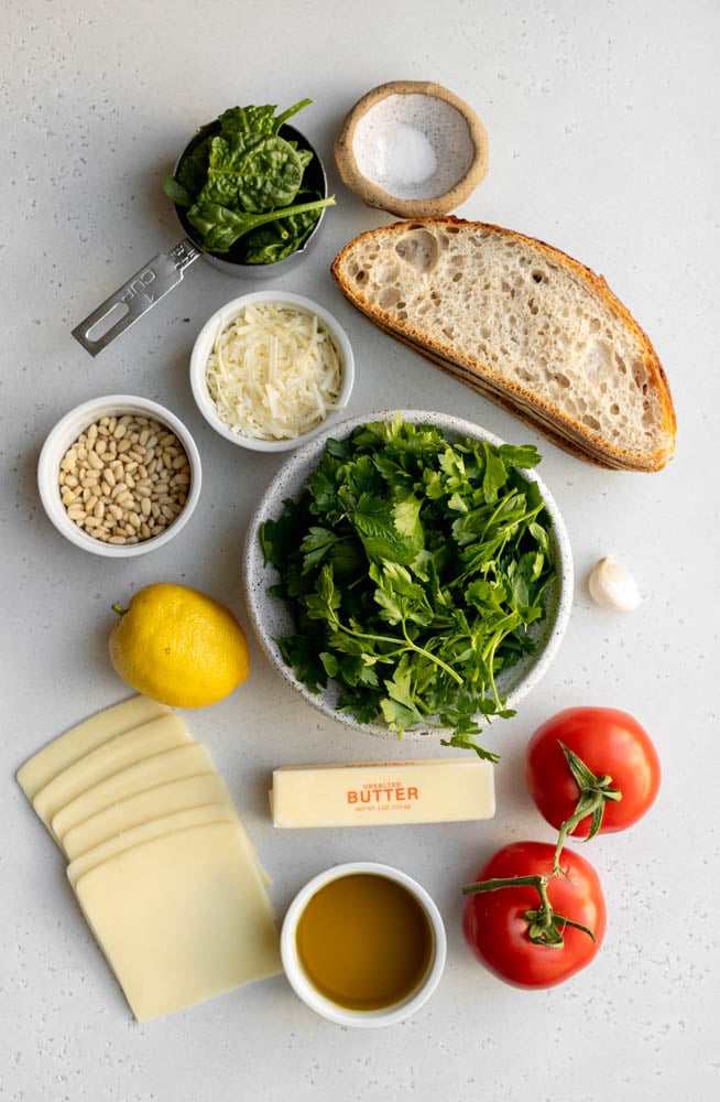ingredients for pesto tomato grilled cheese sandwiches on a light grey backdrop