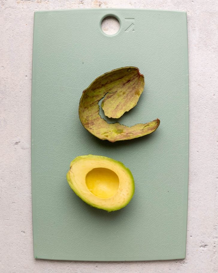 avocado half and peel on a light blue cutting board