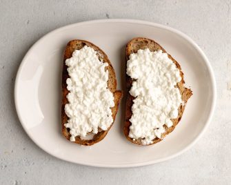 two pieces of toast with cottage cheese spread on top on a white oval plate