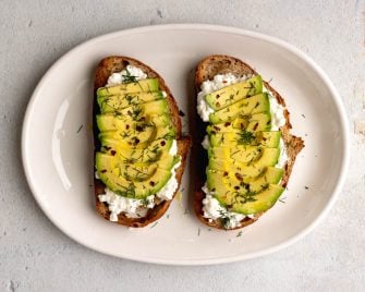 two slices of avocado cottage cheese toast on a white oval plate