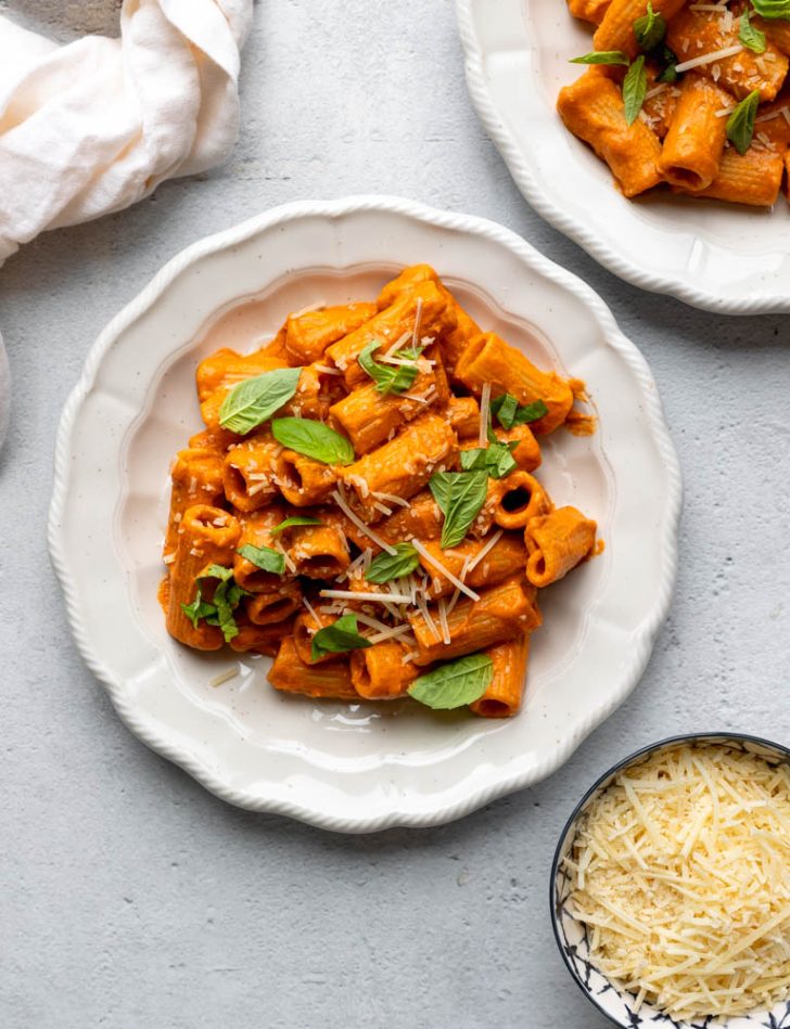 white plate with creamy tomato sauce rigatoni topped with basil leaves and parmesan cheese