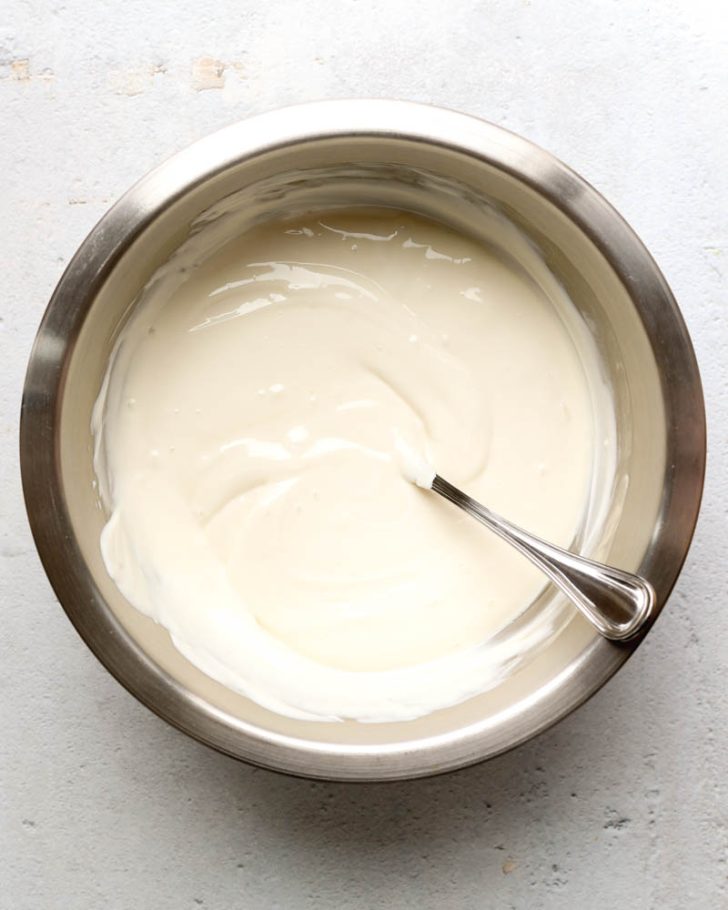 Greek yogurt in a metal mixing bowl with a mixing spoon