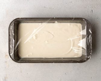 Frozen Greek yogurt in a loaf pan covered with plastic wrap
