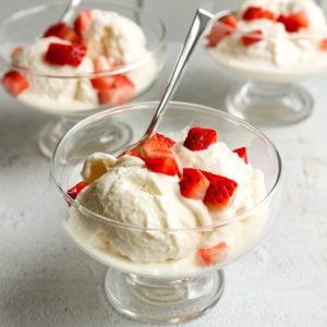 three ice cream bowls with scoops of vanilla greek yogurt topped with chopped strawberries, with small spoons