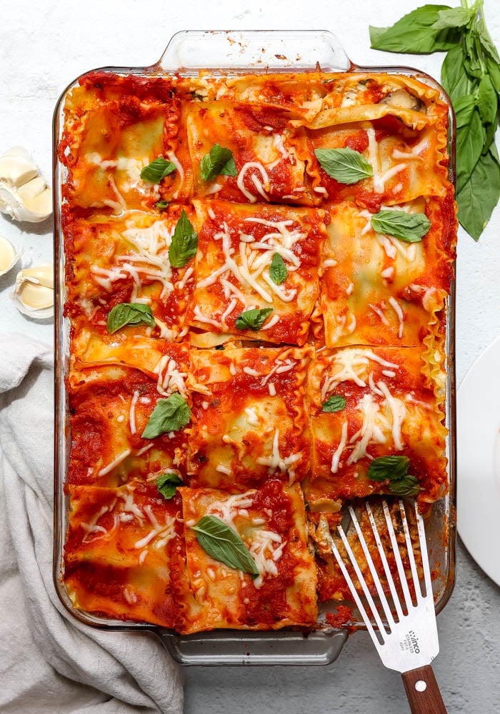 glass pan of lasagna with a spatula removing a piece