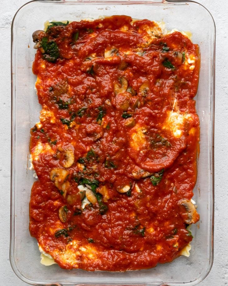 layers of lasagna with sauce in a glass casserole dish