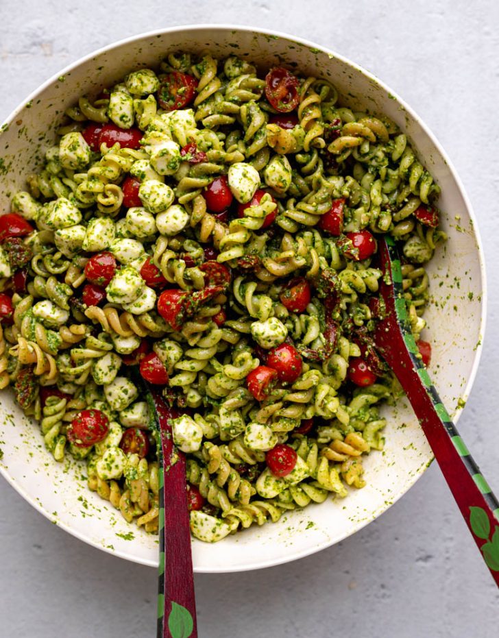 tri color pasta salad in a white mixing bowl with salad spoons