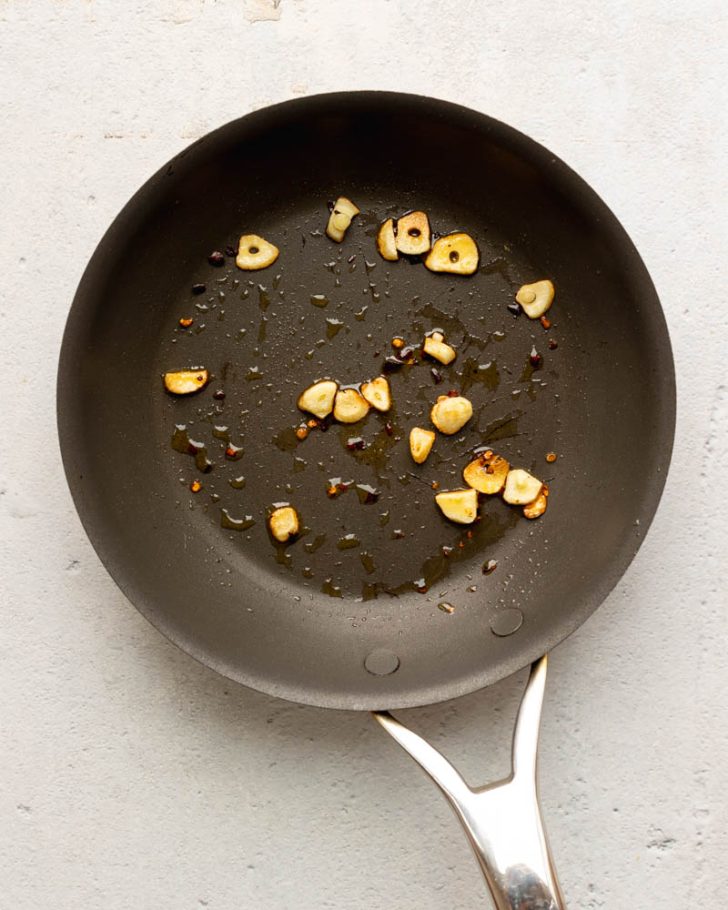 Sliced sauteed garlic in olive oil in a dark nonstick pan