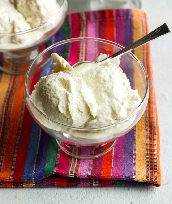 glass ice cream bowl with two scoops of frozen vanilla greek yogurt on a colorful tea towel
