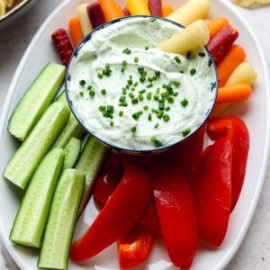 small bowl of veggie dip surrounded by cucumbers, bell pepper, and carrots