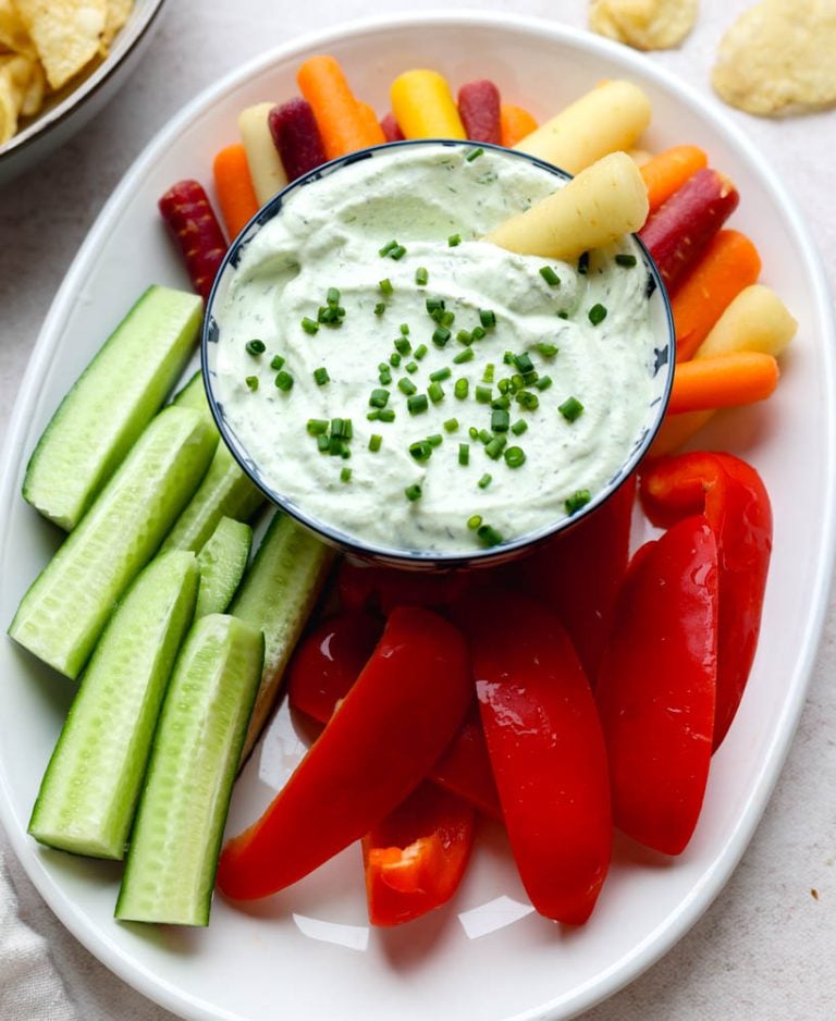 small bowl of veggie dip surrounded by cucumbers, bell pepper, and carrots