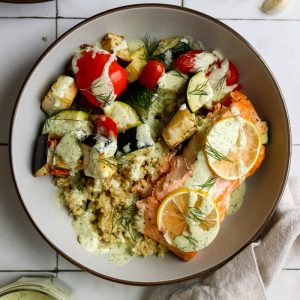 mediterranean salmon quinoa bowl on a white tile backdrop with a jar of sauce off to the side