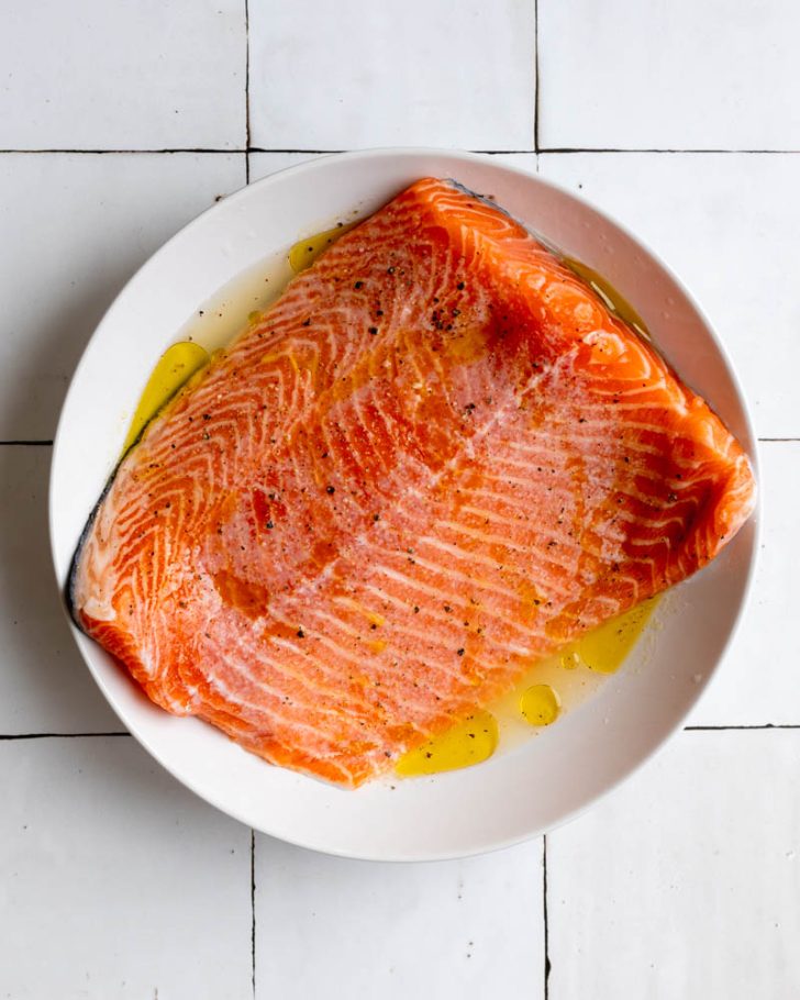 Salmon filet in a white bowl on a white tiled backdrop