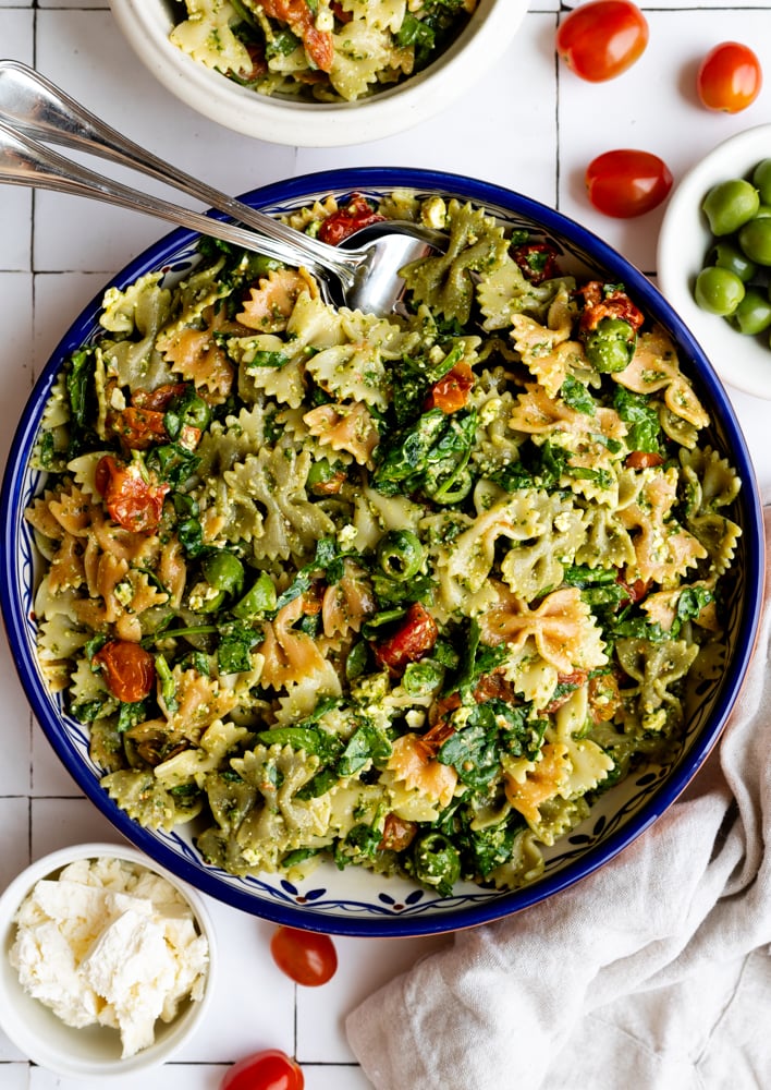 bowtie pasta salad in a colorful blue serving bowl surrounded by some ingredients in small bowls