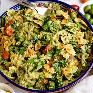 bowtie pasta salad in a colorful blue serving bowl surrounded by some ingredients in small bowls