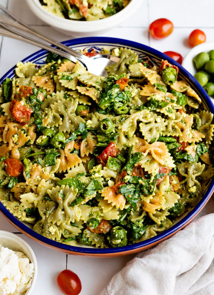 bowtie pasta salad in a colorful blue serving bowl surrounded by some ingredients in small bowls