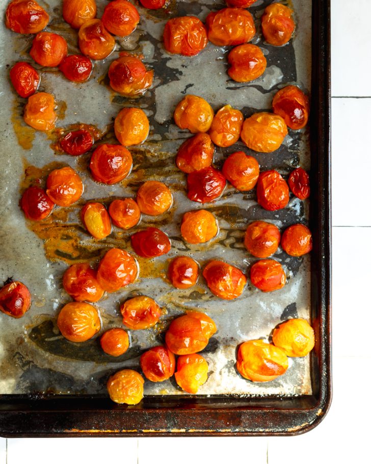 Roasted cherry tomatoes on a parchment paper lined baking sheet