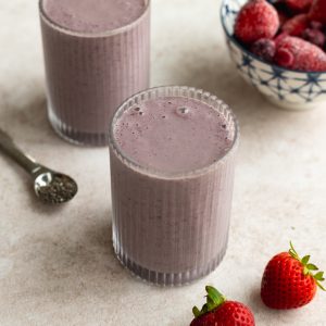 two glasses of greek yogurt smoothie with a bowl of frozen berries beside them