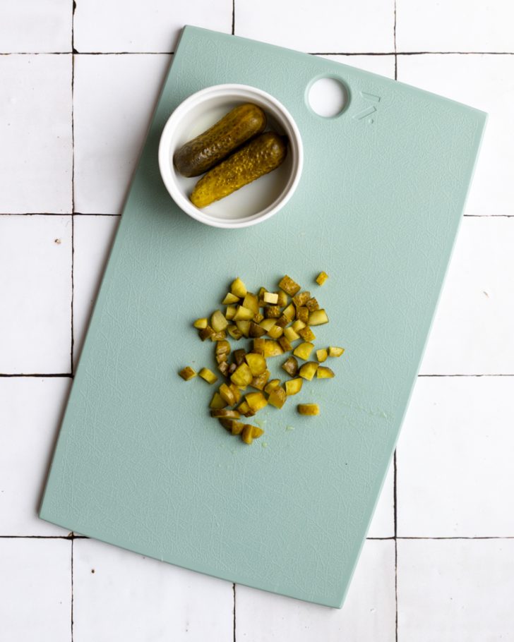 chopped pickle on a blue cutting board with a small dish or pickles