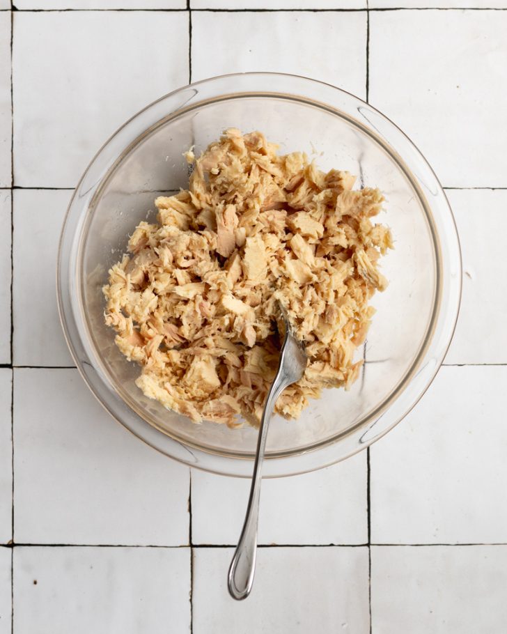 Drained tuna flaked with a fork in a glass bowl