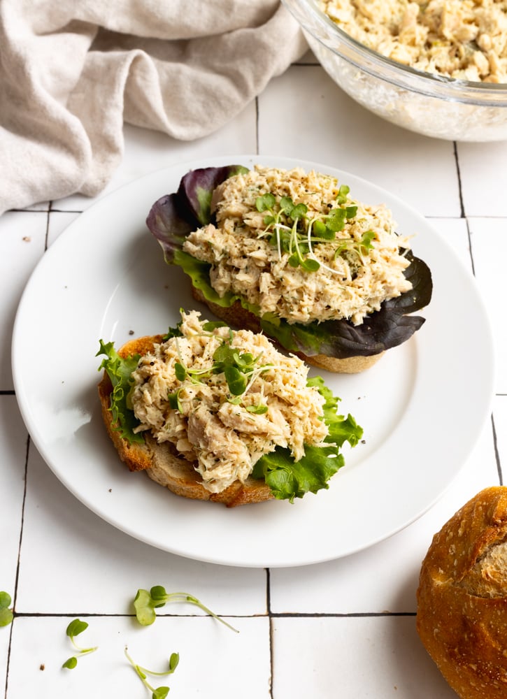 tuna salad with lettuce on sliced bread, on a white plate