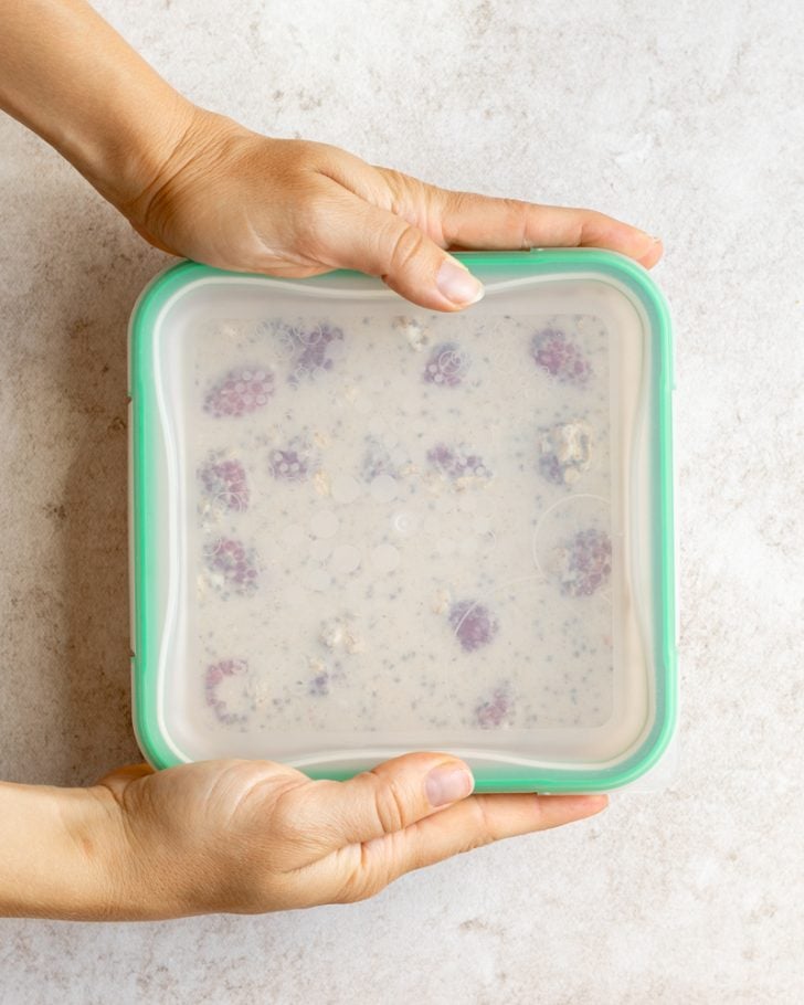 hands covering a square tupperware of overnight oats