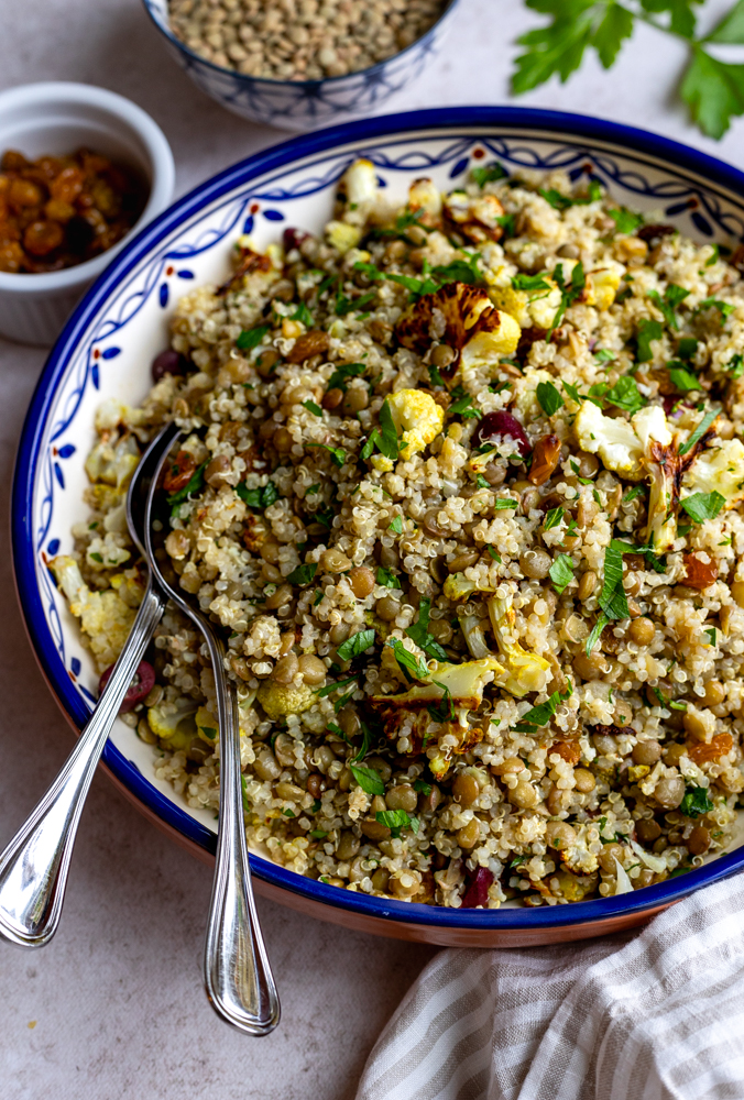 Close up of lentil quinoa salad in a blue rimmed serving bowl with silver serving spoons