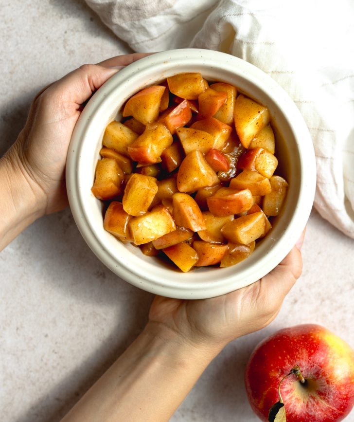 hands cupping a white bowl of stewed apple chunks