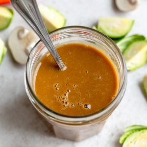 glass jar with vegan stir fry sauce with a silver spoon