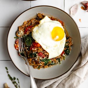 farro grain bowl topped with a fried egg with a silver spoon on a tiled backdrop