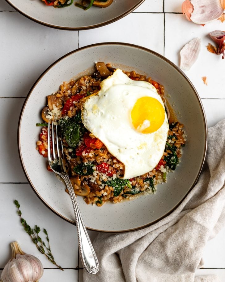 farro grain bowl topped with a fried egg with a silver spoon on a tiled backdrop
