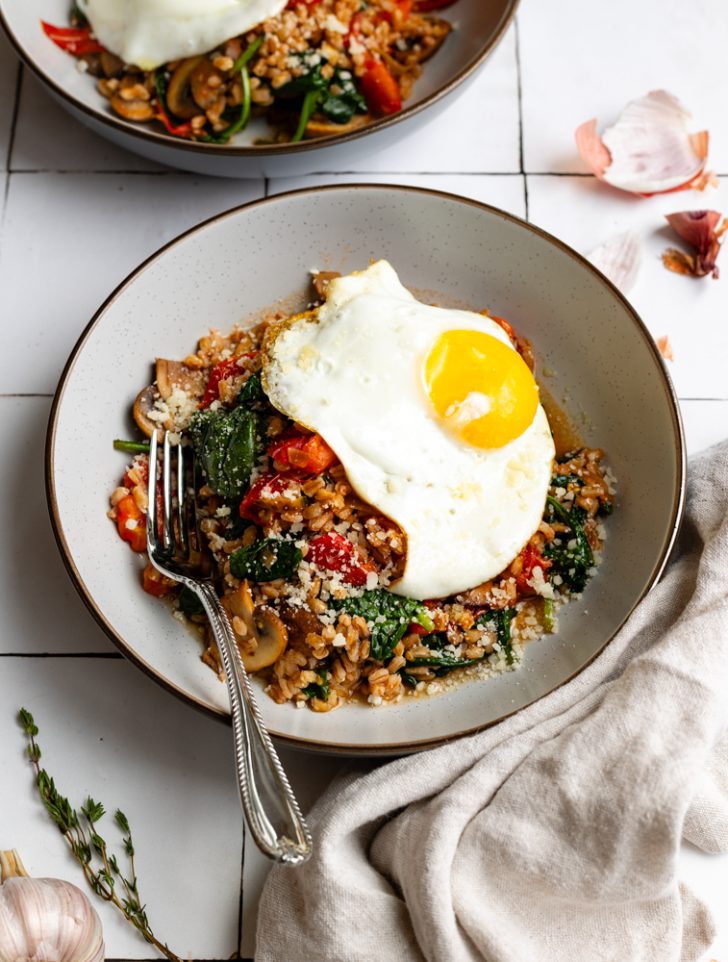 farro grain bowl topped with a fried egg with a silver spoon on a tiled backdrop