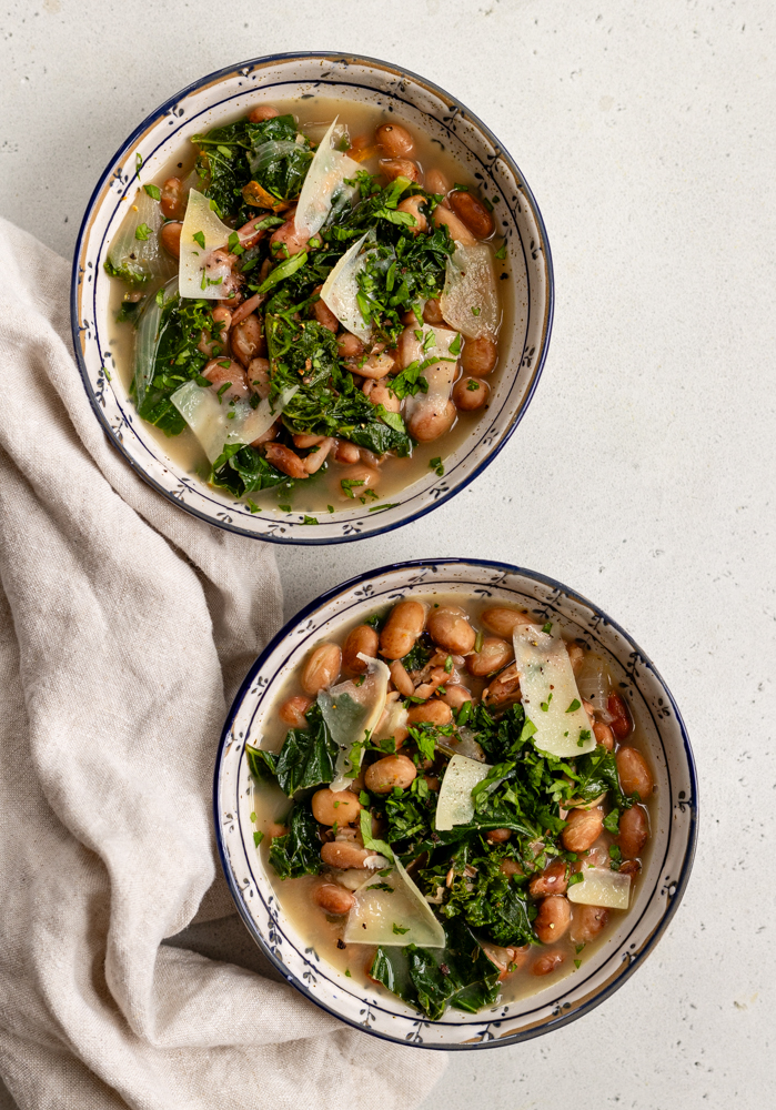 two ceramic bowls of beans and greens next to a linen towel