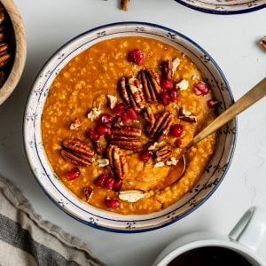 bowl of pumpkin steel cut oats with pomegranate and pecans and a gold spoon