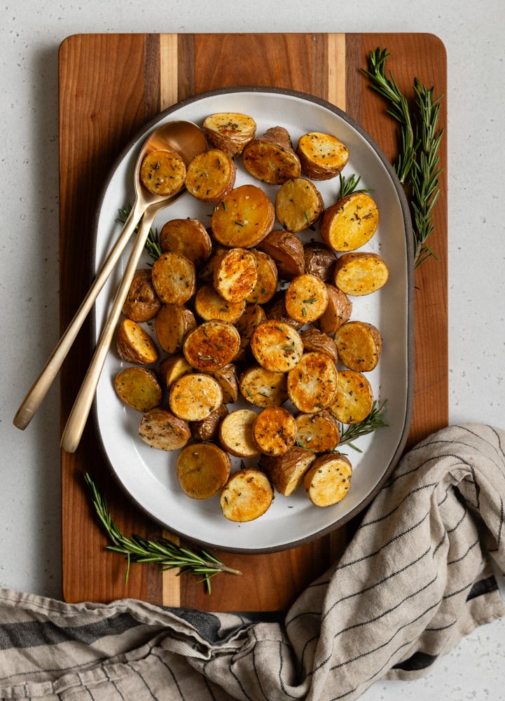 oval platter on a wood board with roasted baby potatoes with gold serving spoons
