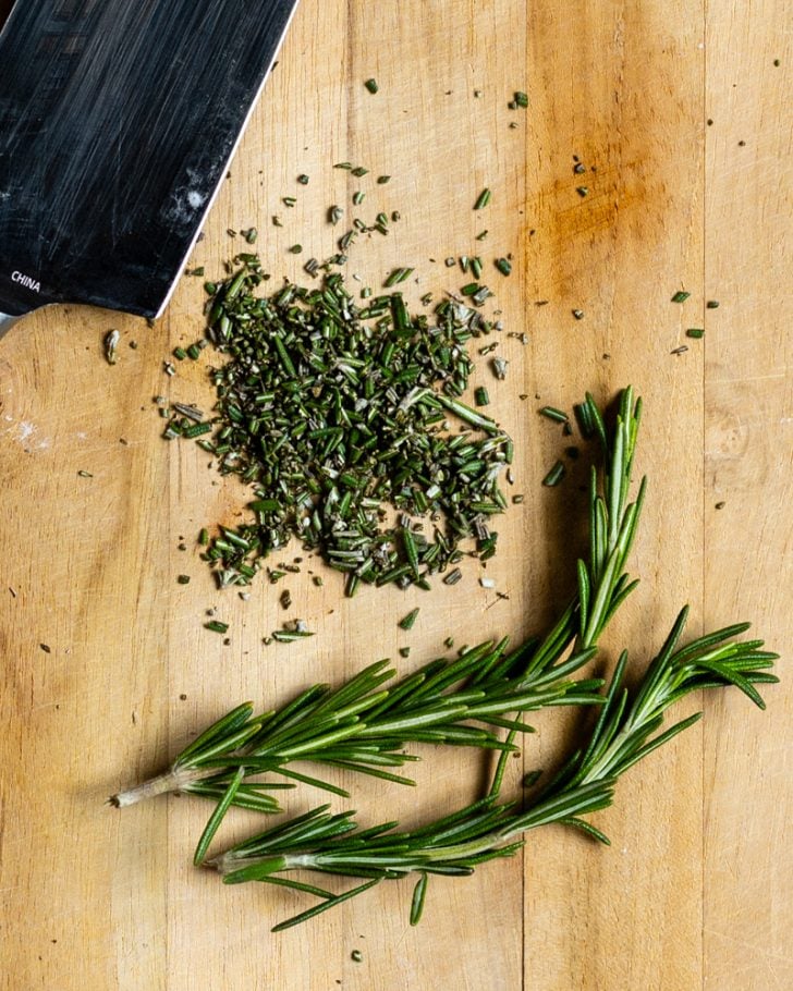 finely chopped rosemary on a wood cutting board next to a few sprigs of fresh rosemary