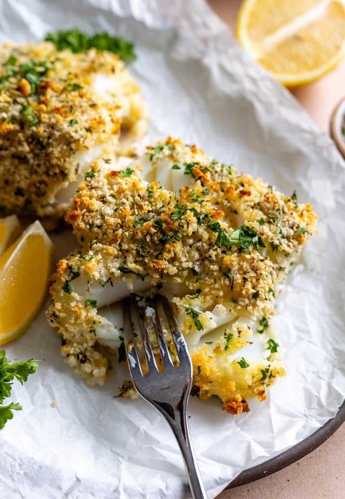 crispy panko crusted baked cod piece on parchment paper with a fork inside