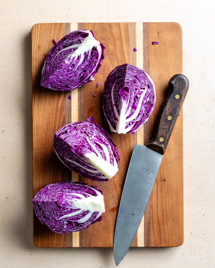 red cabbage cut into 4 wedges on a wood cutting board