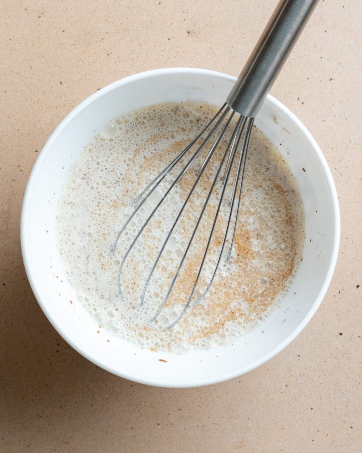 whisked milk in a white bowl with a silver whisk