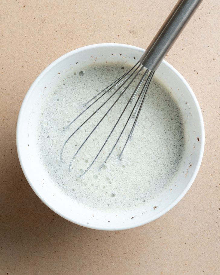 chia pudding whisked in a white bowl with a silver whisk