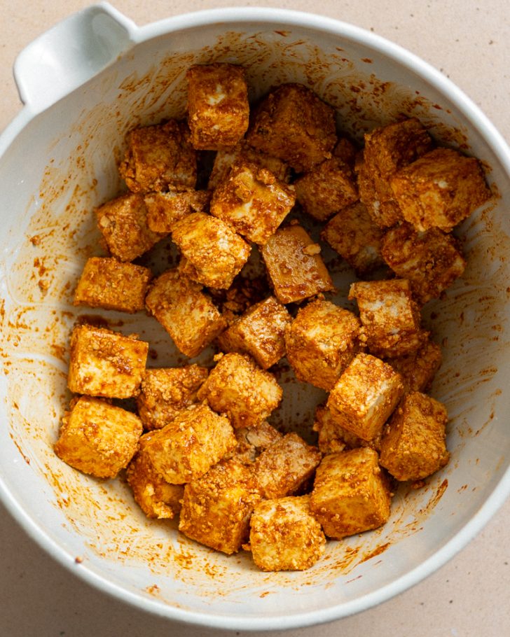 tofu tossed in seasonings in a mixing bowl