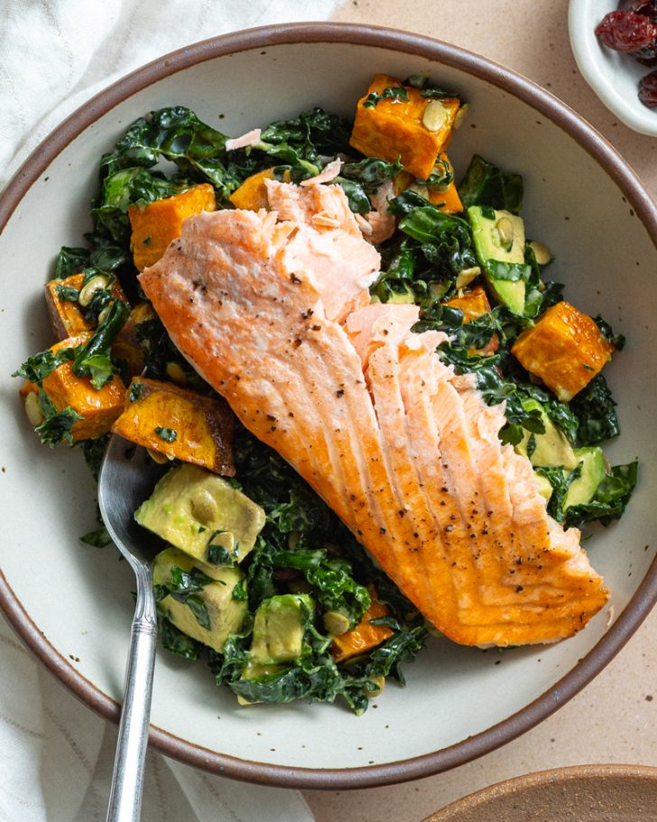 kale salad in a bowl with a piece of baked salmon on top